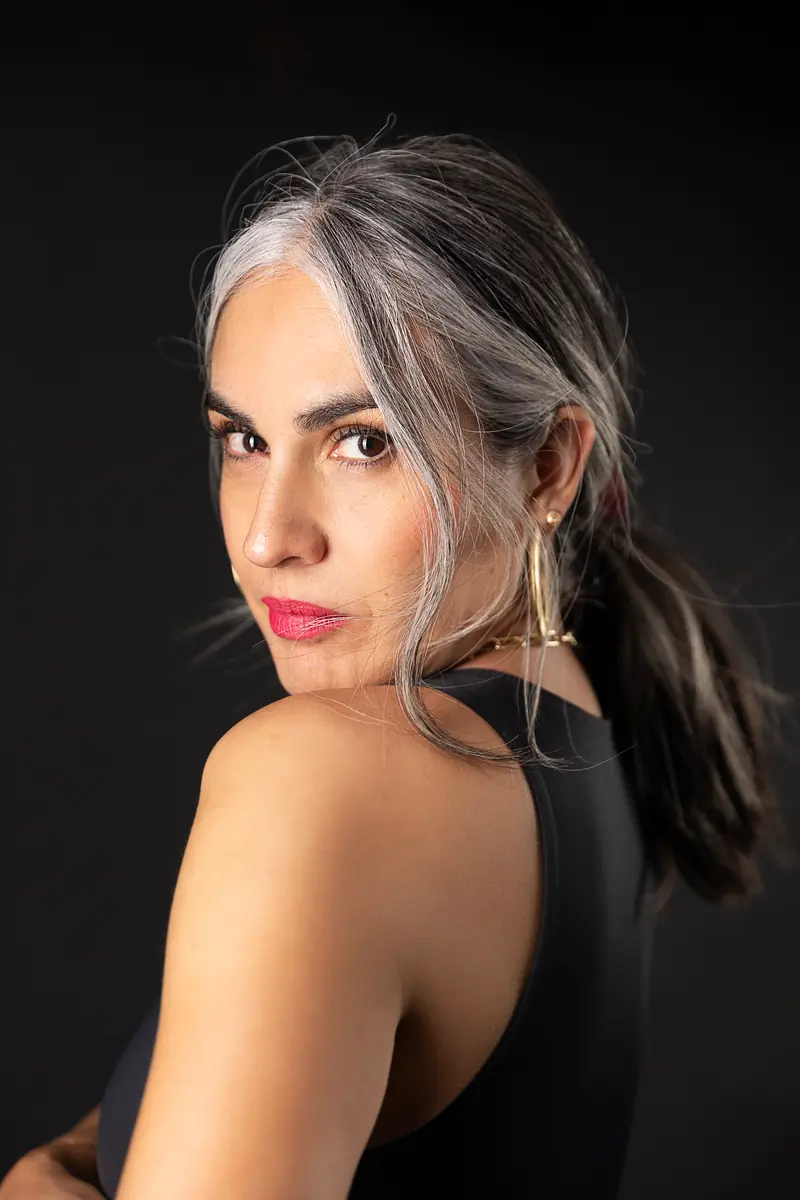 Retrato de Pili Valencia sobre fondo negro, mirando de frente por encima del hombro.